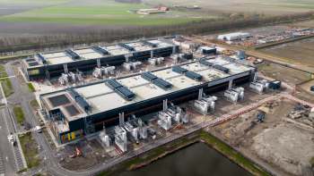 An aerial view of a large data center facility under construction, surrounded by fields and machinery.