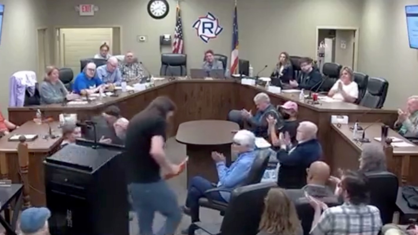 A public meeting room with attendees applauding after a man leaves the podium after speaking.