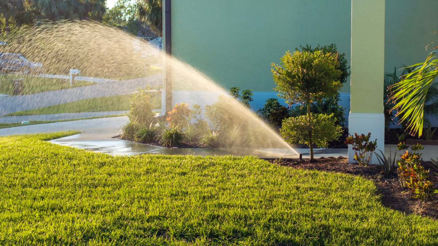 A residential lawn being watered by a sprinkler with vibrant green grass and shrubs in the foreground.