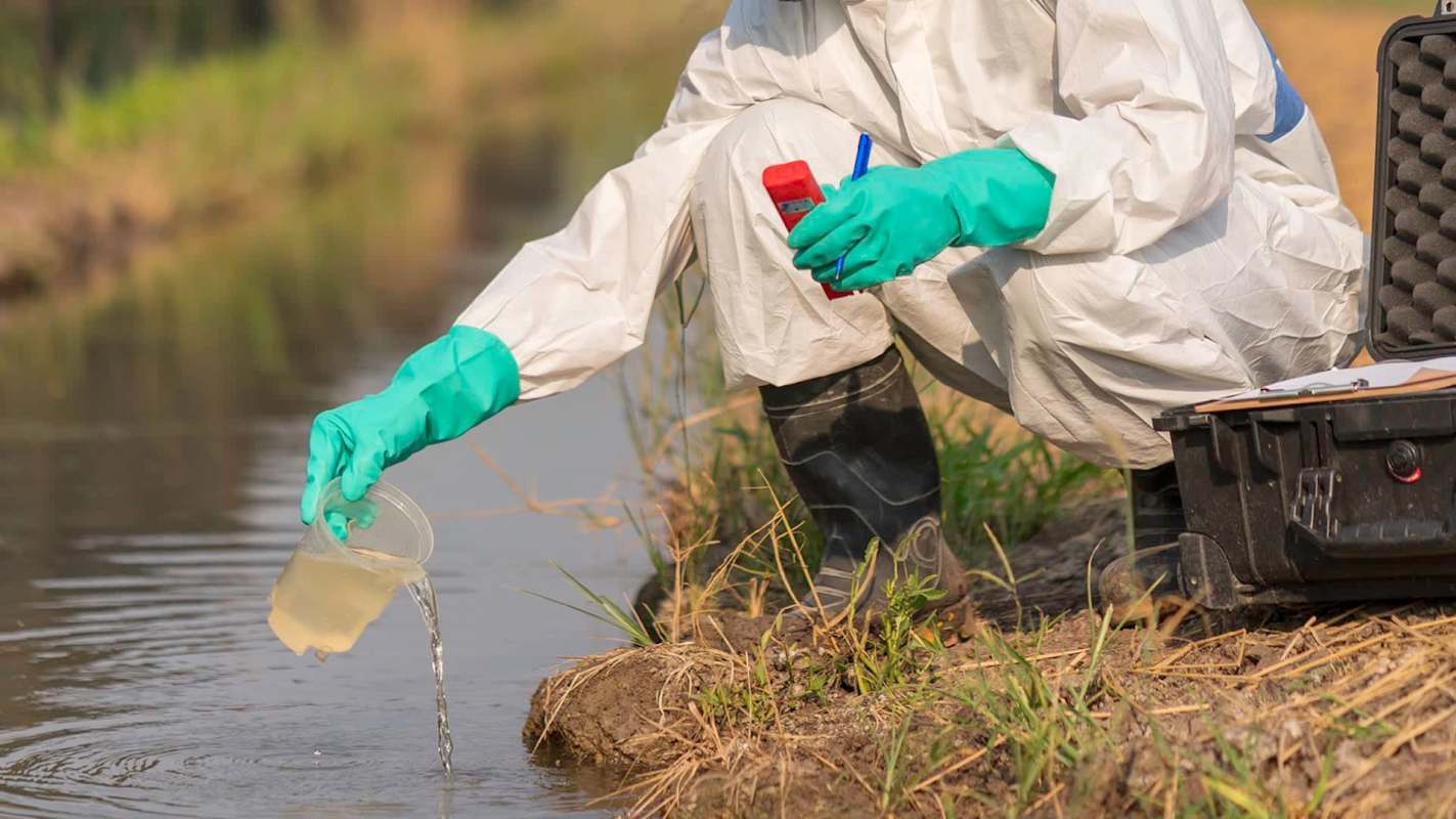 A person in protective gear collects water samples from a stream.