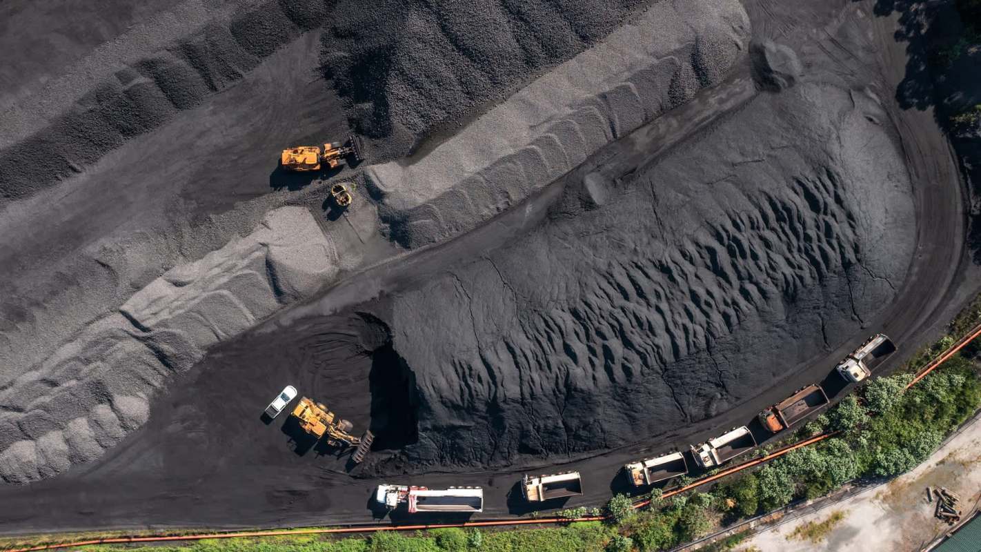 An aerial view of a coal yard with trucks and heavy machinery working on large piles of black coal.