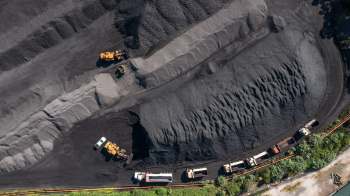 An aerial view of a coal yard with trucks and heavy machinery working on large piles of black coal.