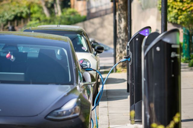 Two electric cars are parked near charging stations with cables connected for power.