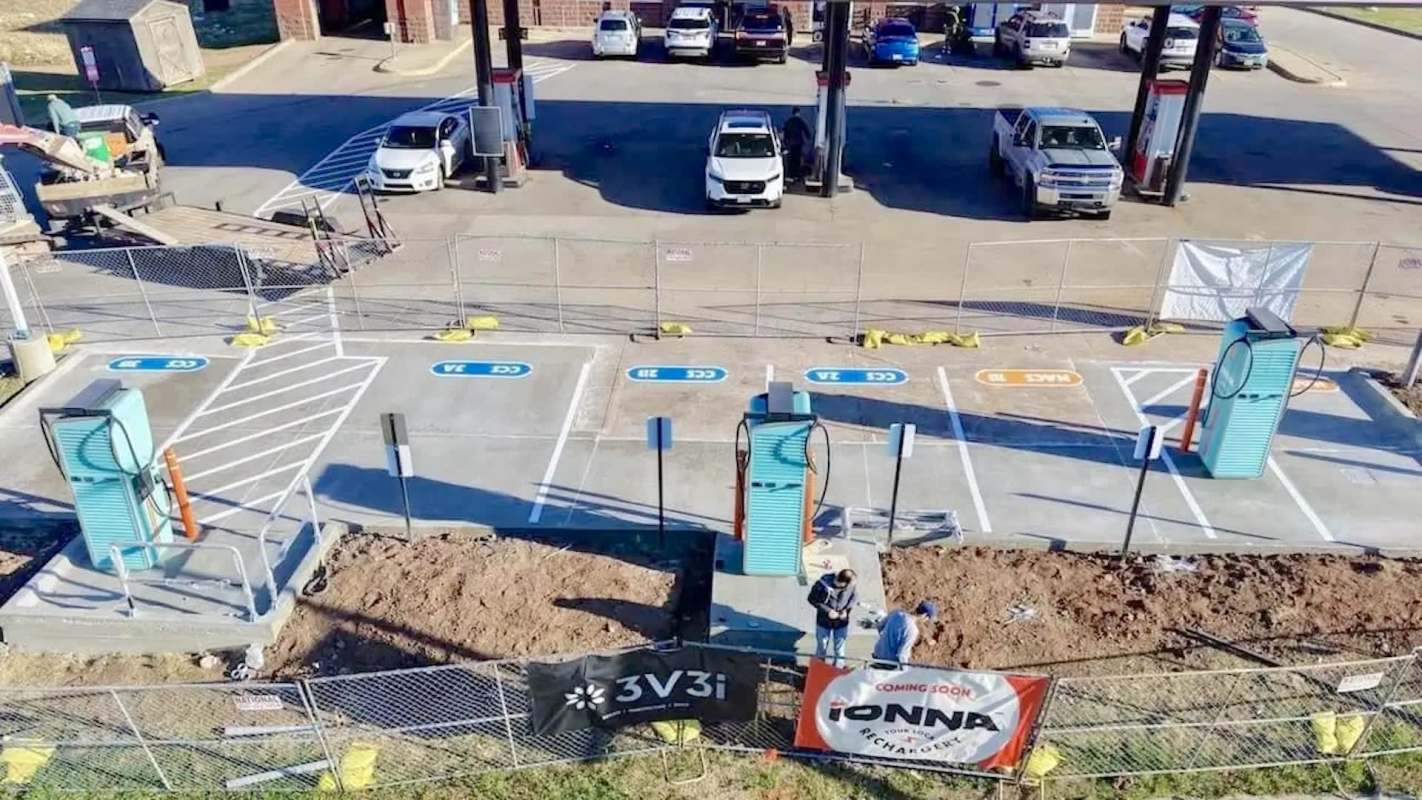 A construction site with electric vehicle charging stations being installed, featuring workers and parked vehicles nearby.
