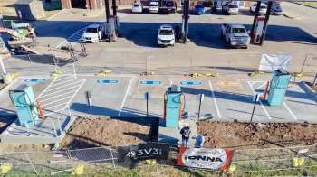 A construction site with electric vehicle charging stations being installed, featuring workers and parked vehicles nearby.