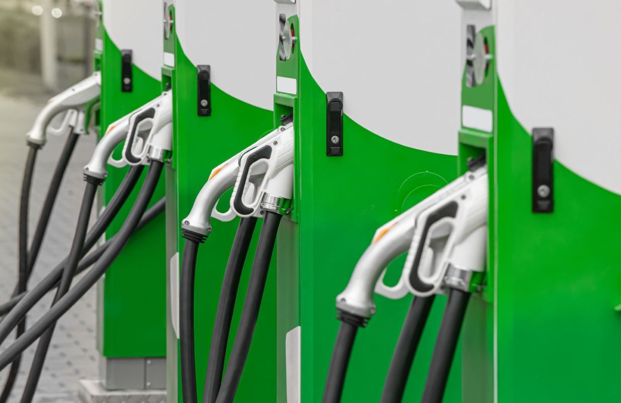 A row of green fuel pumps with nozzles and hoses at a service station.