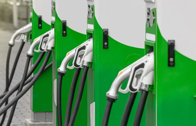 A row of green fuel pumps with nozzles and hoses at a service station.