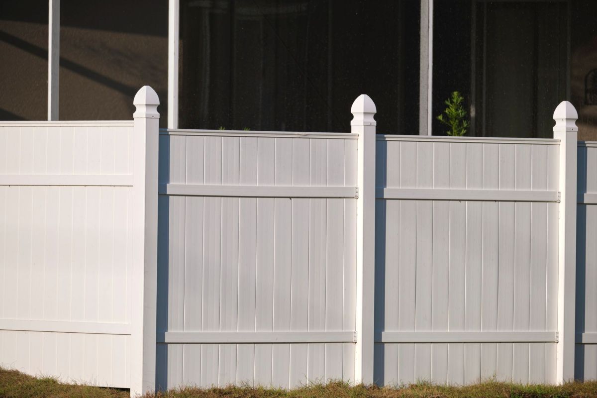A white vinyl fence in front of a dark house.