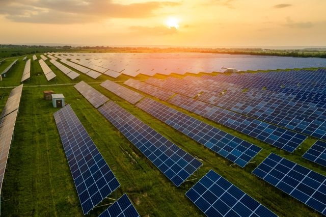 A wide view of a solar farm with numerous solar panels against a sunset backdrop.