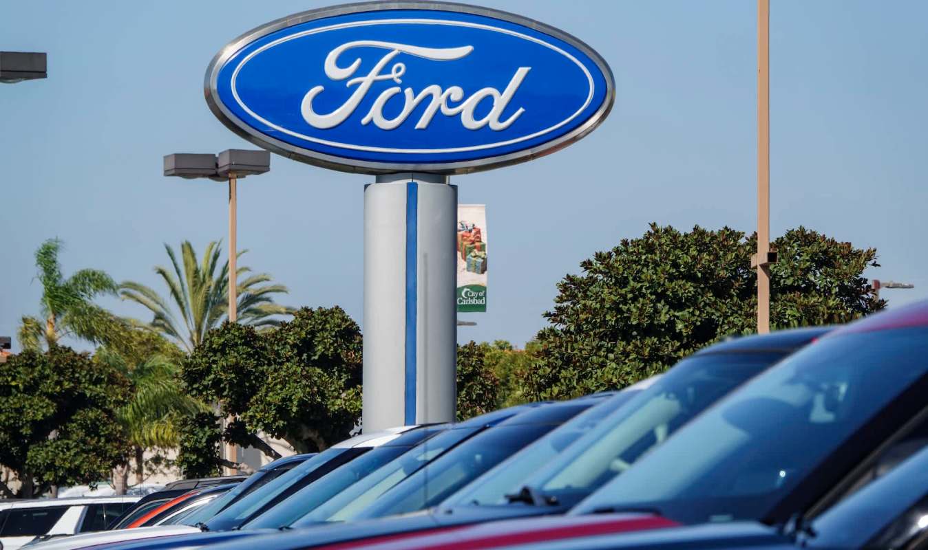 A row of cars in a dealership with a prominent Ford sign and palm trees in the background.