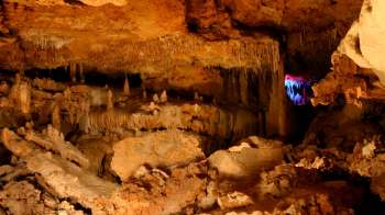 A dimly lit cave featuring intricate rock formations and colorful lighting illuminating the background.