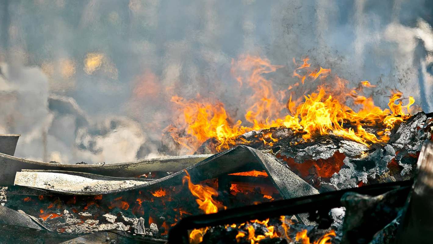 Flames and smoke engulf charred debris in a fiery scene, illustrating destruction and heat.