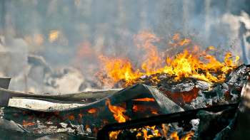 Flames and smoke engulf charred debris in a fiery scene, illustrating destruction and heat.