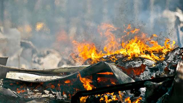Flames and smoke engulf charred debris in a fiery scene, illustrating destruction and heat.