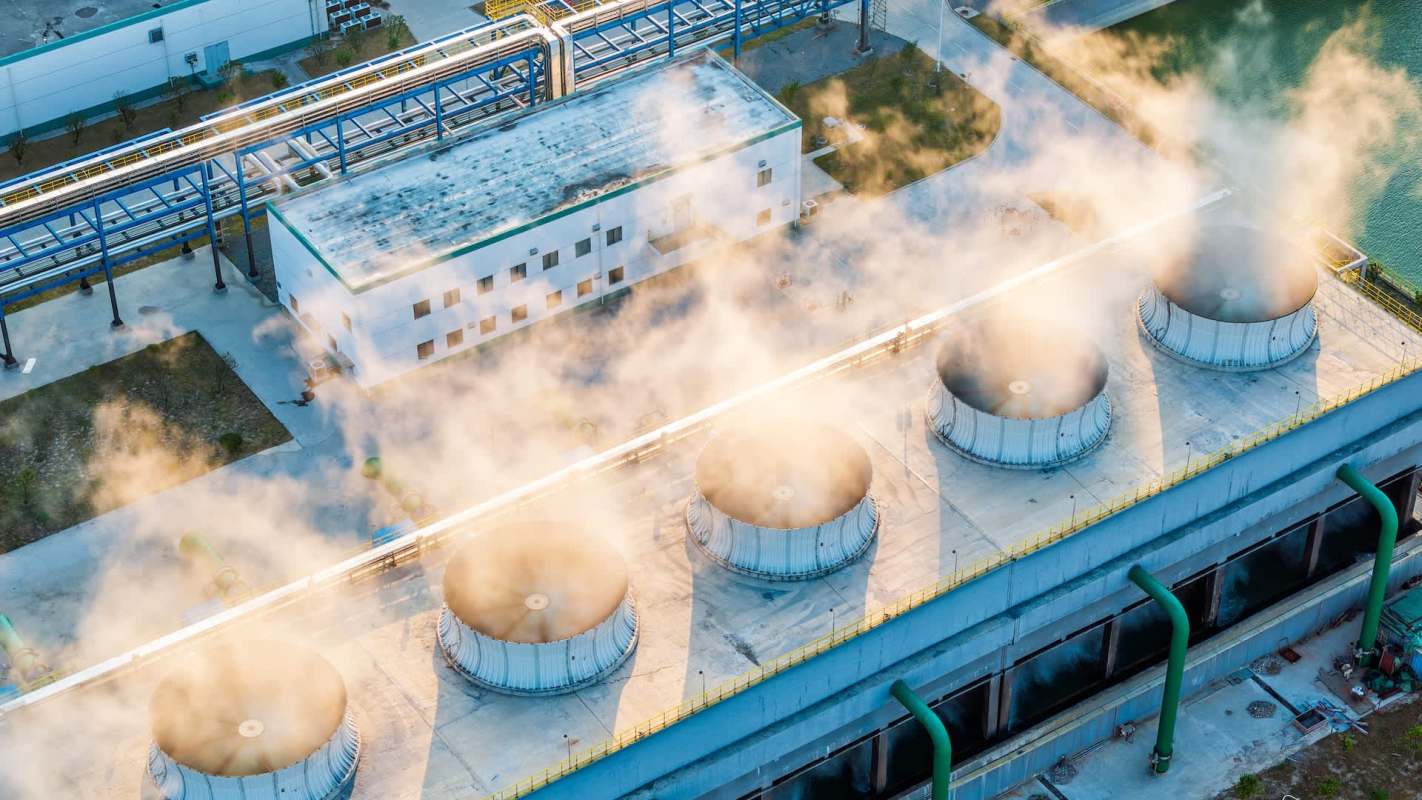 Aerial view of cooling towers emitting steam near an industrial facility.
