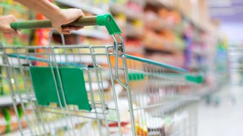 A person pushing a shopping cart through a grocery store aisle filled with colorful products.