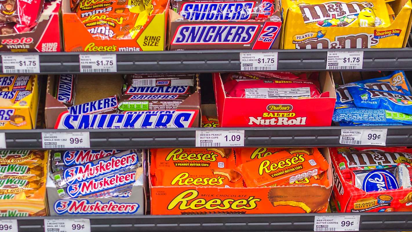 A colorful display of various candy bars and packs, including Reese's, Snickers, and M&M's, on store shelves.