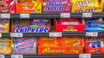 A colorful display of various candy bars and packs, including Reese's, Snickers, and M&M's, on store shelves.