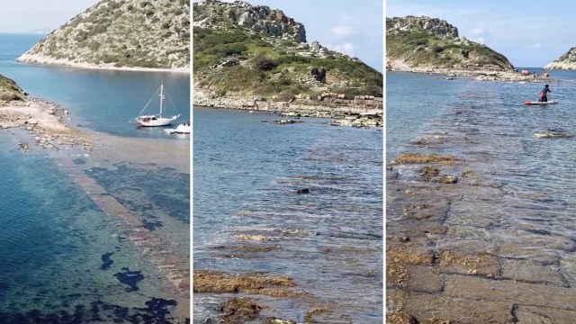 A rocky coastline with a visible ancient pathway leading into clear water, featuring boats and lush green hills.