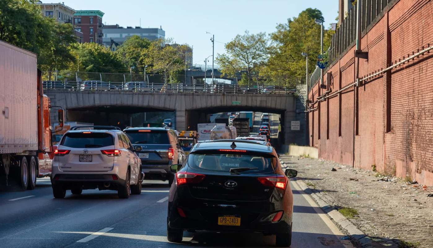 A view of a busy highway with cars, overhead bridge, and buildings surrounded by greenery.