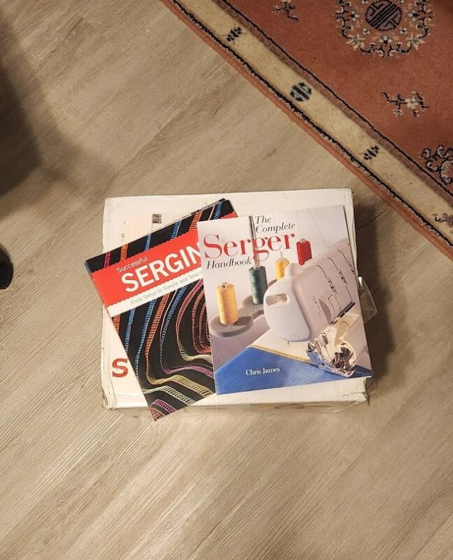 The manual for a Singer Serger sewing machine on top of a box.