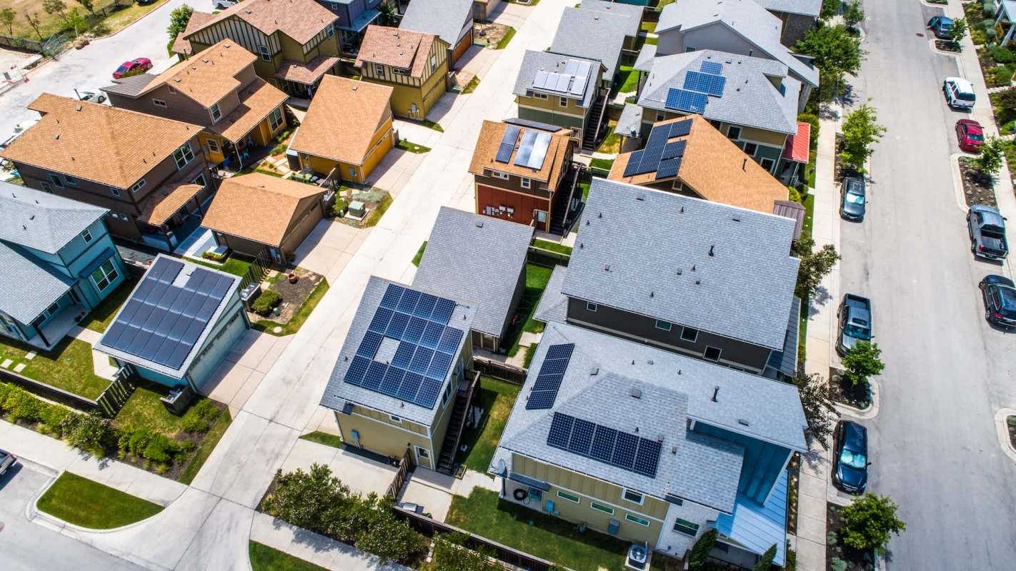 An aerial view of a neighborhood featuring several homes with solar panels on their roofs.