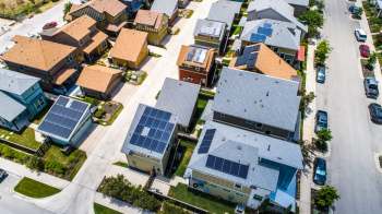 An aerial view of a neighborhood featuring several homes with solar panels on their roofs.