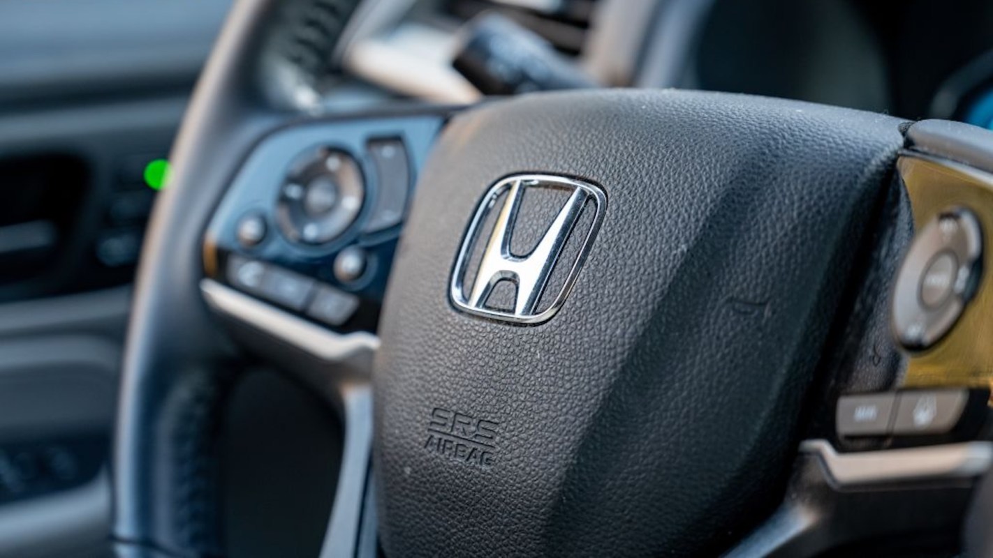 A close-up of a black Honda steering wheel with controls and the Honda logo prominently displayed.