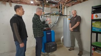 Three men converse in a basement with a heating system, discussing its features and functionality.