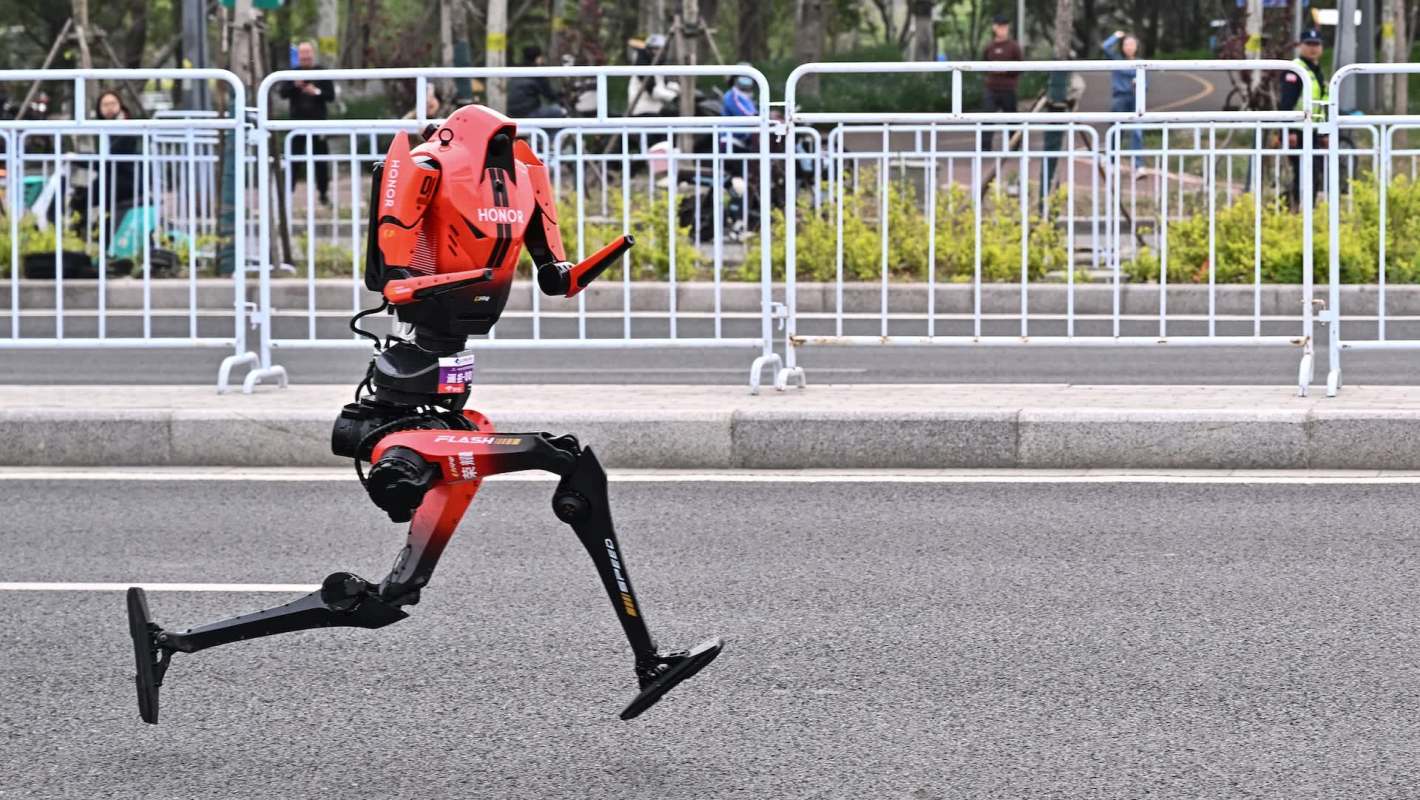 A robotic figure with a motorboat design runs along a road, surrounded by spectators and barriers.