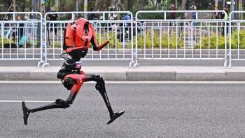 A robotic figure with a motorboat design runs along a road, surrounded by spectators and barriers.