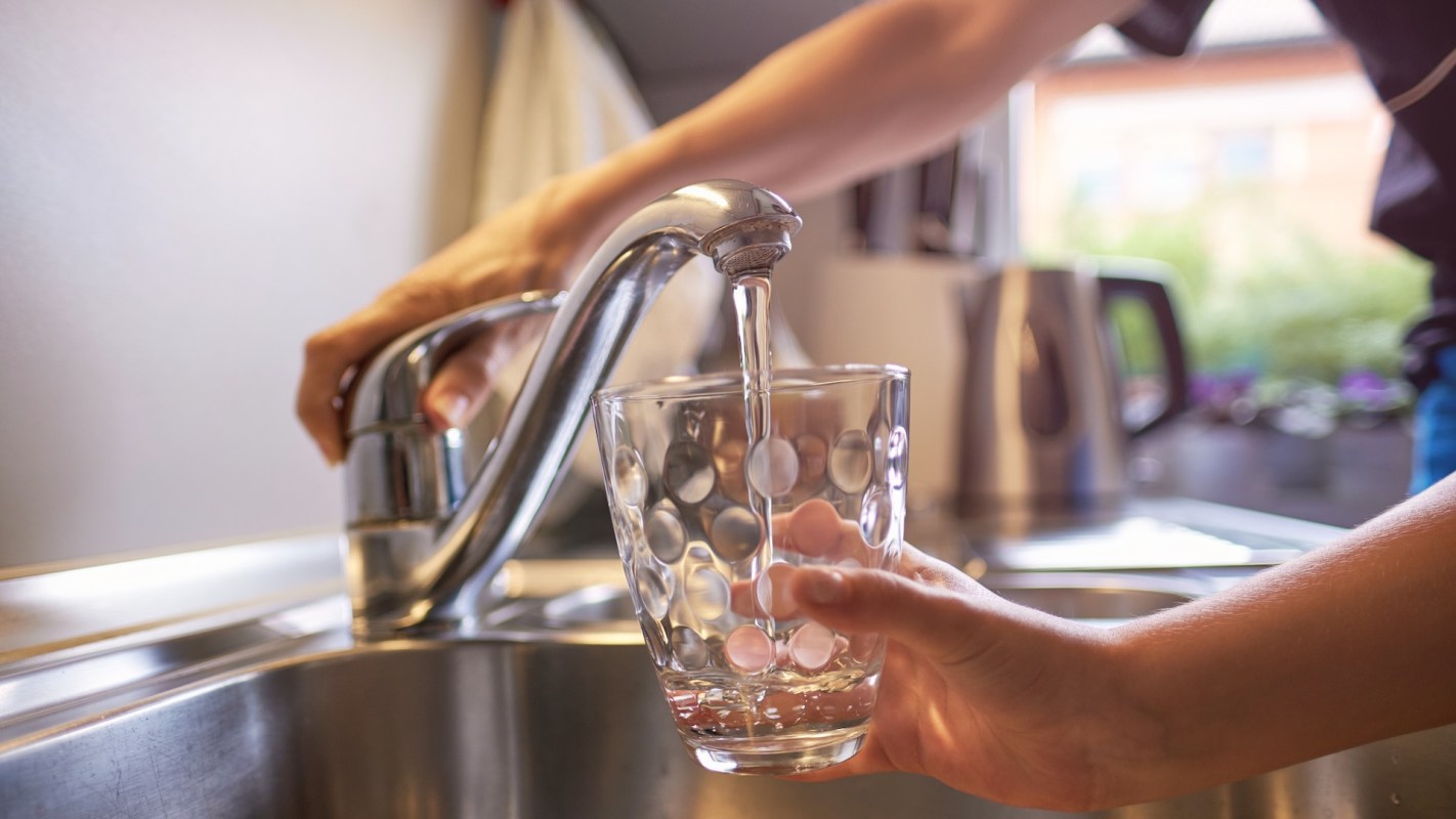 A person fills a clear glass with water from a kitchen faucet.