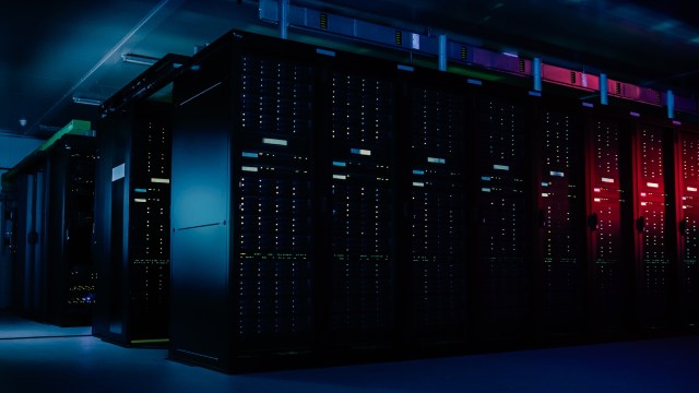 A dimly lit server room filled with tall black server racks illuminated by colorful LEDs.
