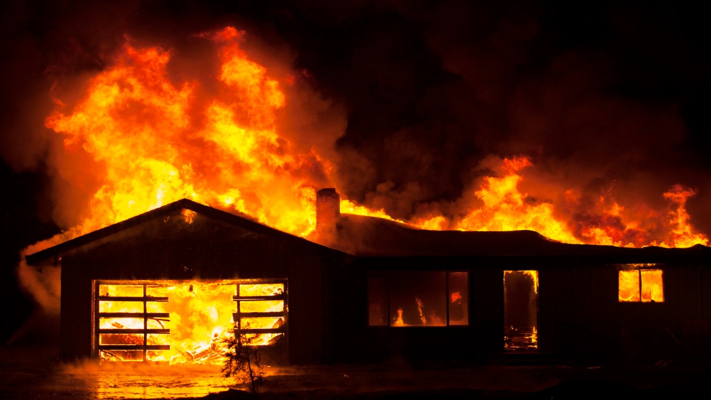 A residential home at night on fire and fully engulfed.