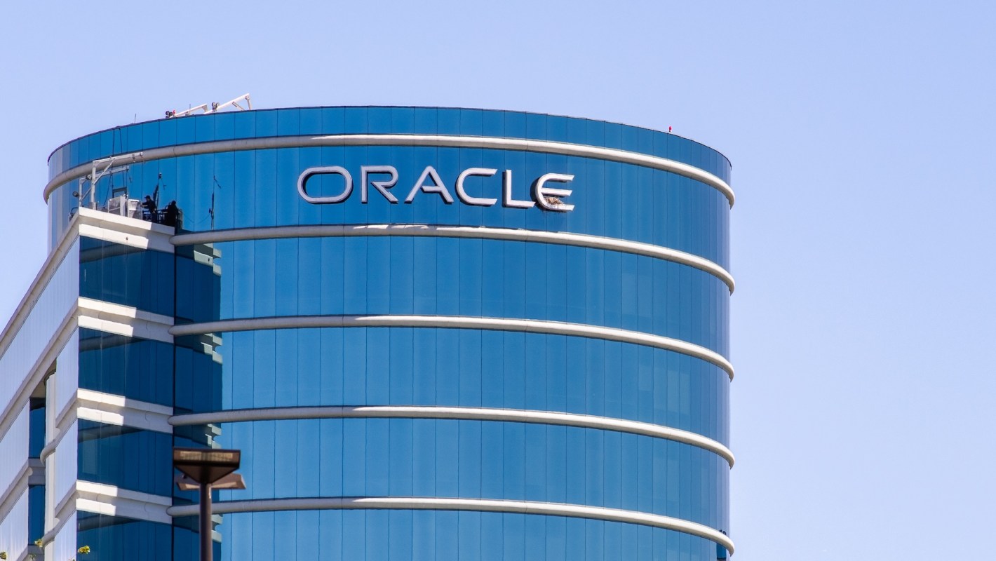 A close-up of a modern skyscraper featuring the “Oracle” logo on its blue, reflective facade.