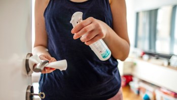 A person cleaning a door handle with a spray cleaner and a cloth in a well-lit room.