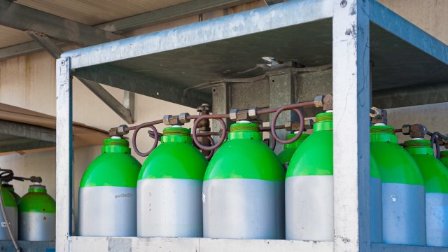 A rack of green and silver gas cylinders connected by pipes in a storage area.