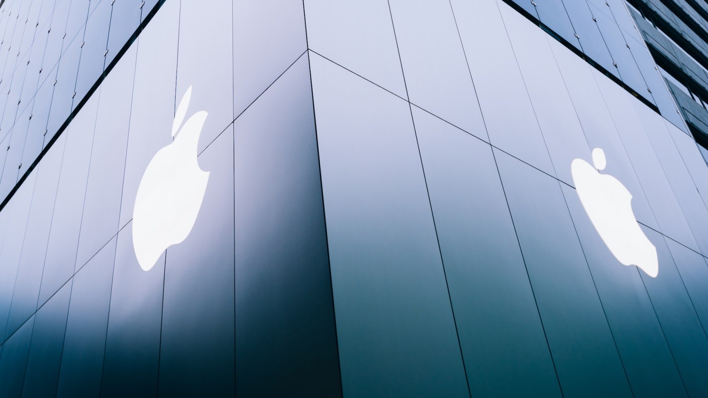A close-up angle of a modern glass building featuring two illuminated Apple logos on its facade.