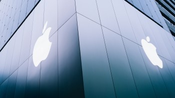 A close-up angle of a modern glass building featuring two illuminated Apple logos on its facade.