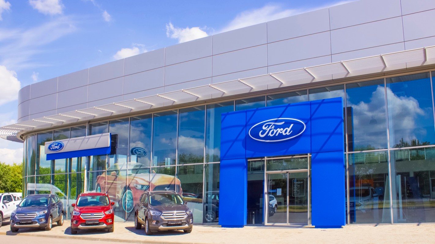 A modern Ford dealership showcasing several vehicles outside and a large blue Ford sign on the building.