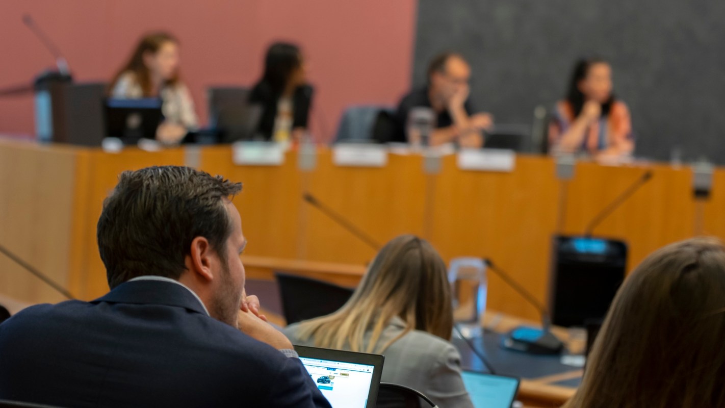 A group of people attending a meeting, with one participant focused on a laptop in the foreground.