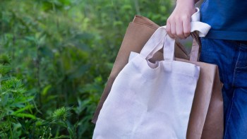 A person holds reusable shopping bags while standing in a green, natural setting.