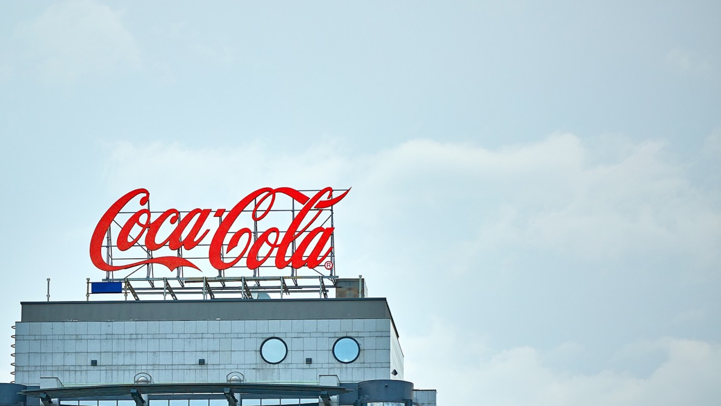 A large red Coca-Cola sign atop a modern building against a clear sky.