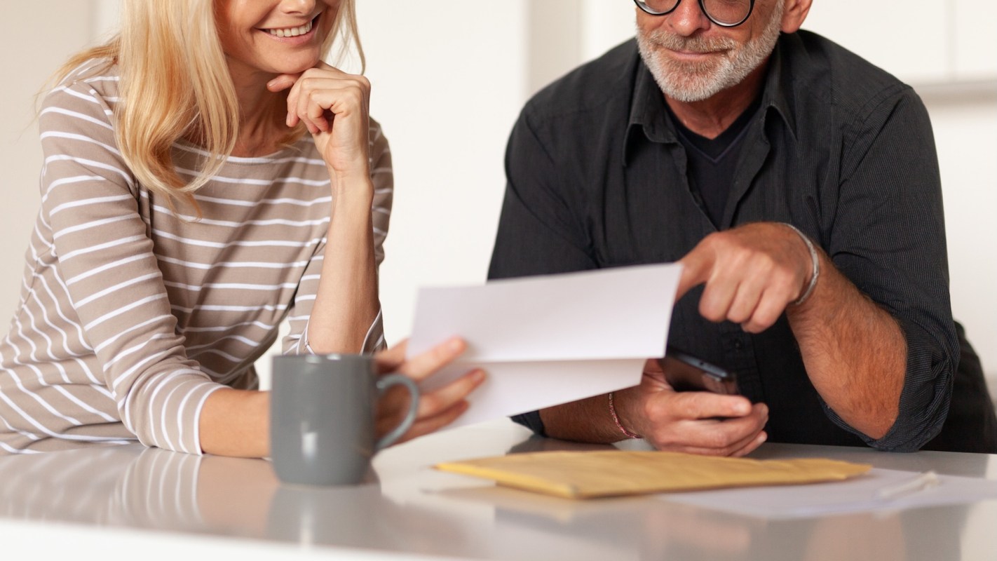 A woman and man discuss papers at a table, with the woman smiling and holding a coffee mug.