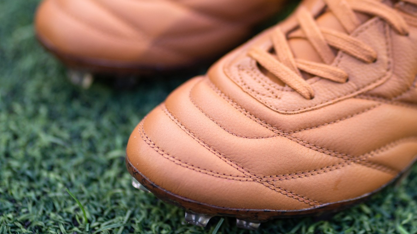 A close-up of a brown soccer cleat resting on artificial grass.