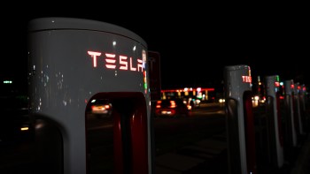 A row of illuminated Tesla charging stations at night, with blurred car lights in the background.