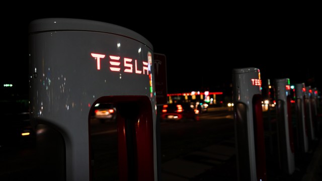 A row of illuminated Tesla charging stations at night, with blurred car lights in the background.