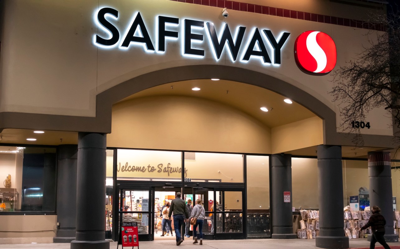 A group of people approaching a Safeway grocery store entrance at night, illuminated by its sign.
