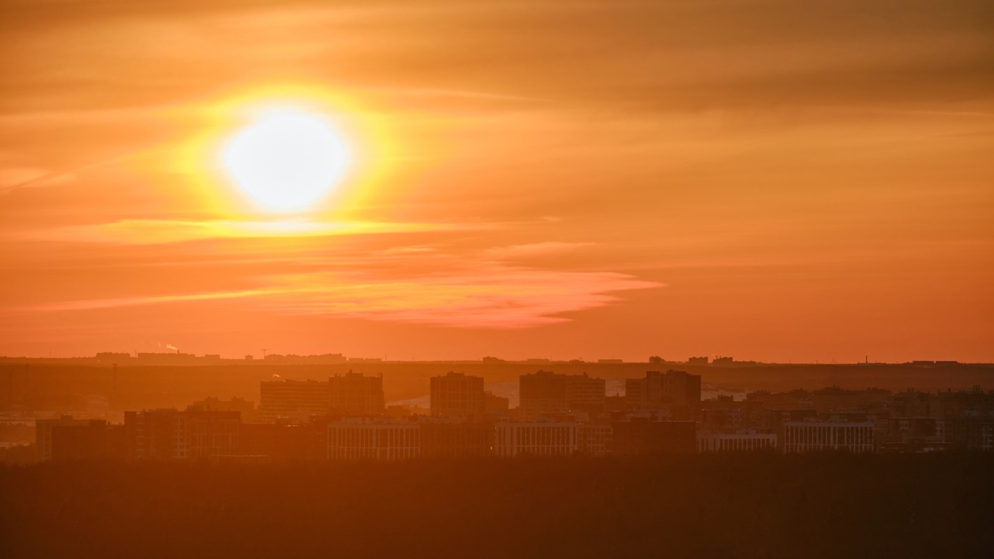 A vibrant sunset casts orange hues over silhouetted urban buildings.