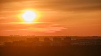 A vibrant sunset casts orange hues over silhouetted urban buildings.